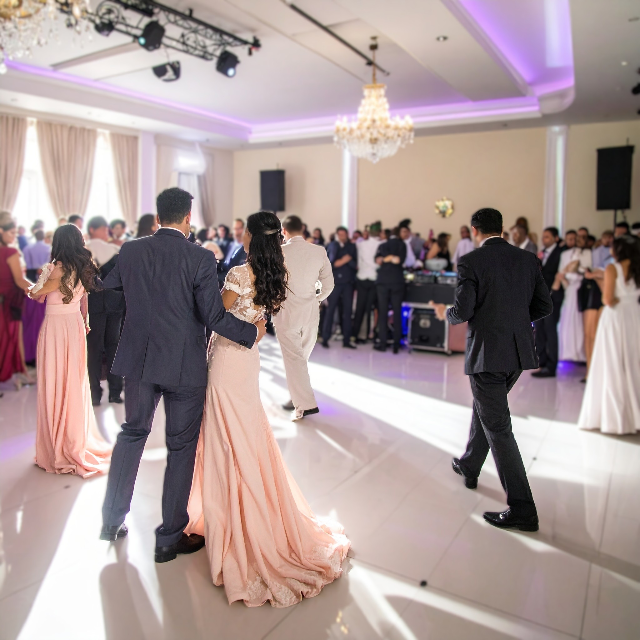 couple de mariés enlacés sur le dancefloor, salle blanche avec lustre et ambiance violette