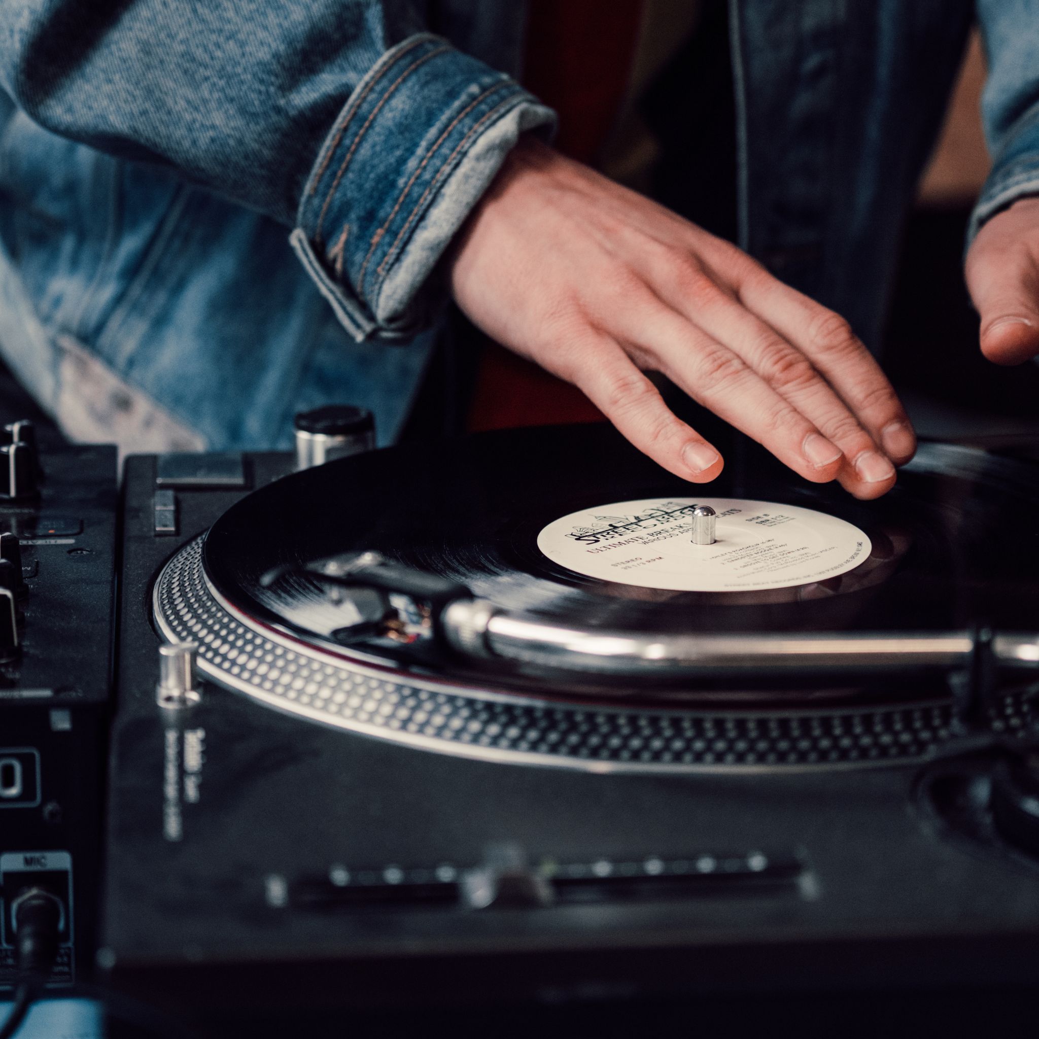 gros plan sur une platine vinyle avec disque en rotation et main de DJ qui mixe en soiree