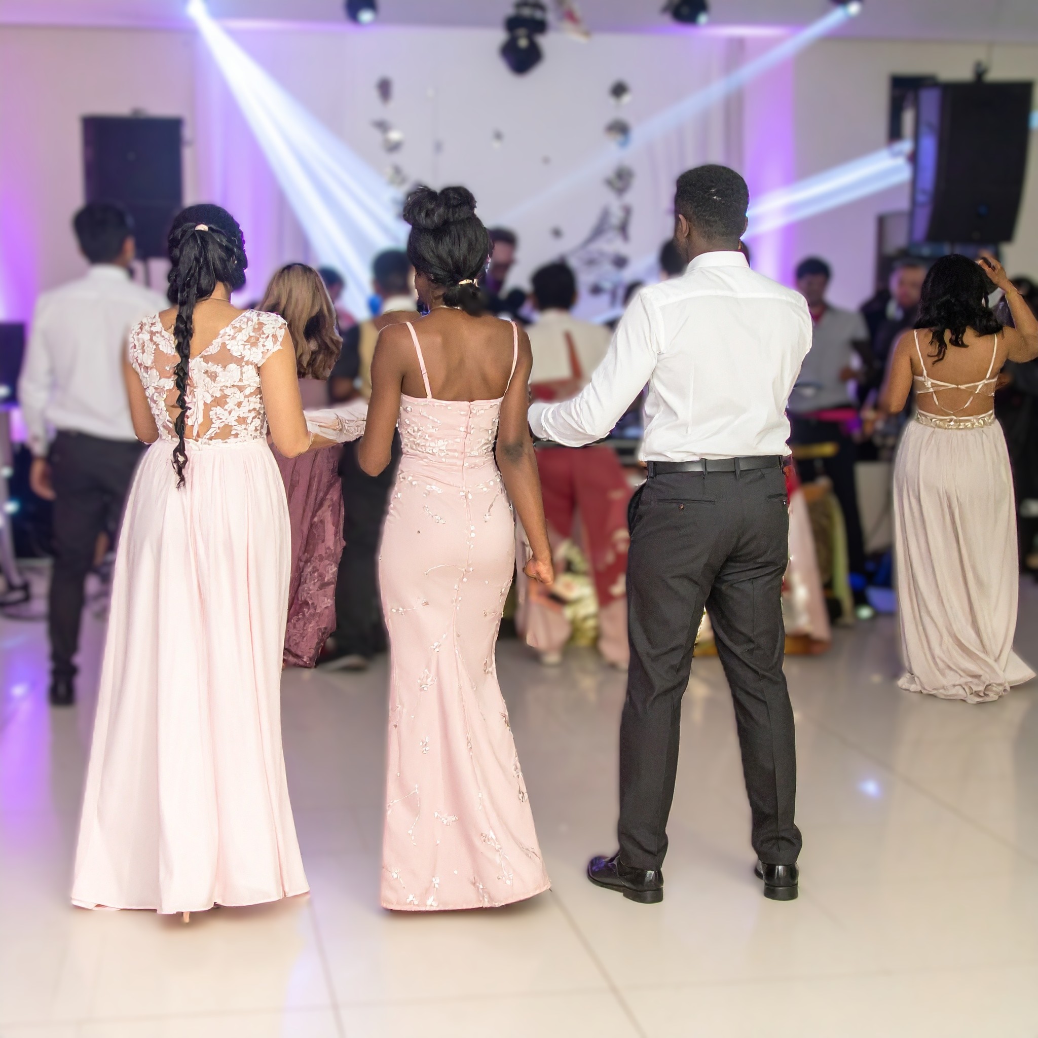 invités d'un mariage mixte en robes longues qui dansent sous les jeux de lumière du DJ