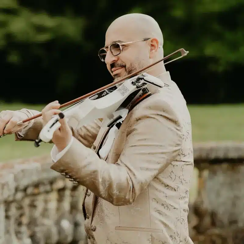Tarek, violoniste live de l'équipe DJ Dadicool, jouant du violon électrique en costume crème brocardé doré lors d'un cocktail mariage extérieur